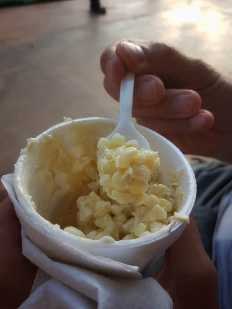 throw away cup of corn covered in mayo and cheese. Hand holding spoonful of corn