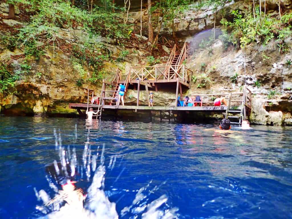 view of a cenote from the water. a splash in front of photos. wooden platform and stairs. people on platform