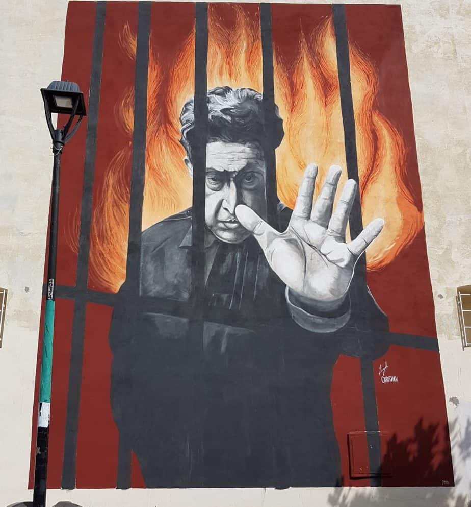 mural of a man behind bars with fire behind him. hand coming out of bars
