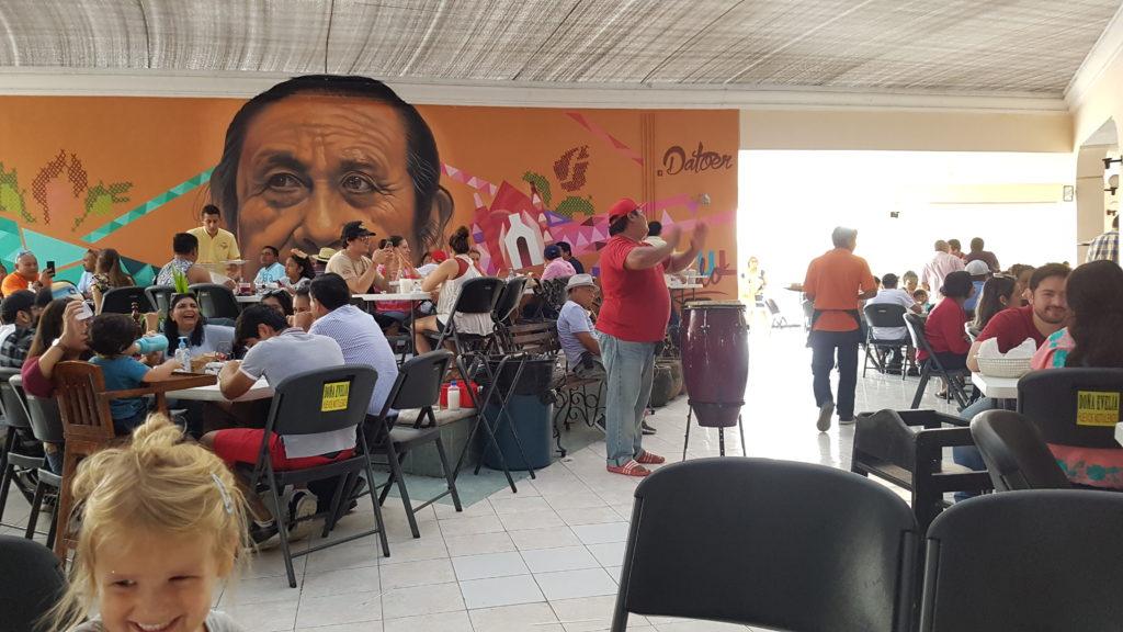 busy restaurant scene with mural of a persons face on back wall