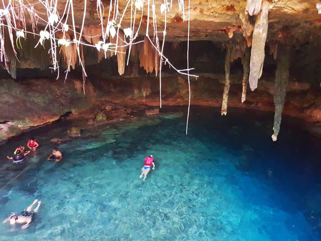 cave cenote, very blue water, person in red life jacket, vines hangings 
