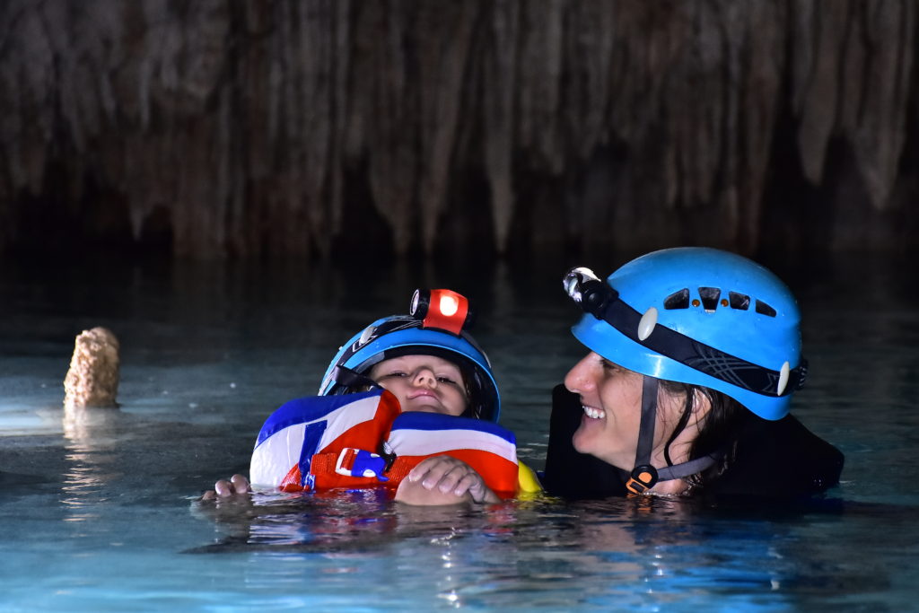 parent and child swimming ini a cave. Both wearing life jackets and helmets