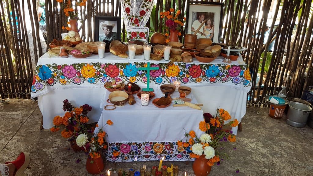 Beautifully decorated altar with white table cloths and food and drink with photos of the dead.