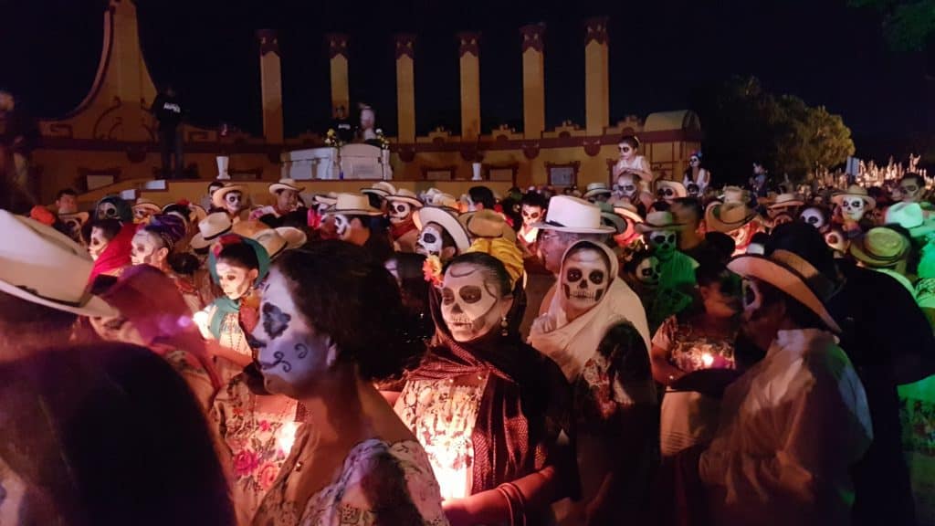 People with white skull facepaint, holding candles and walking in procession for Day of the Dead
