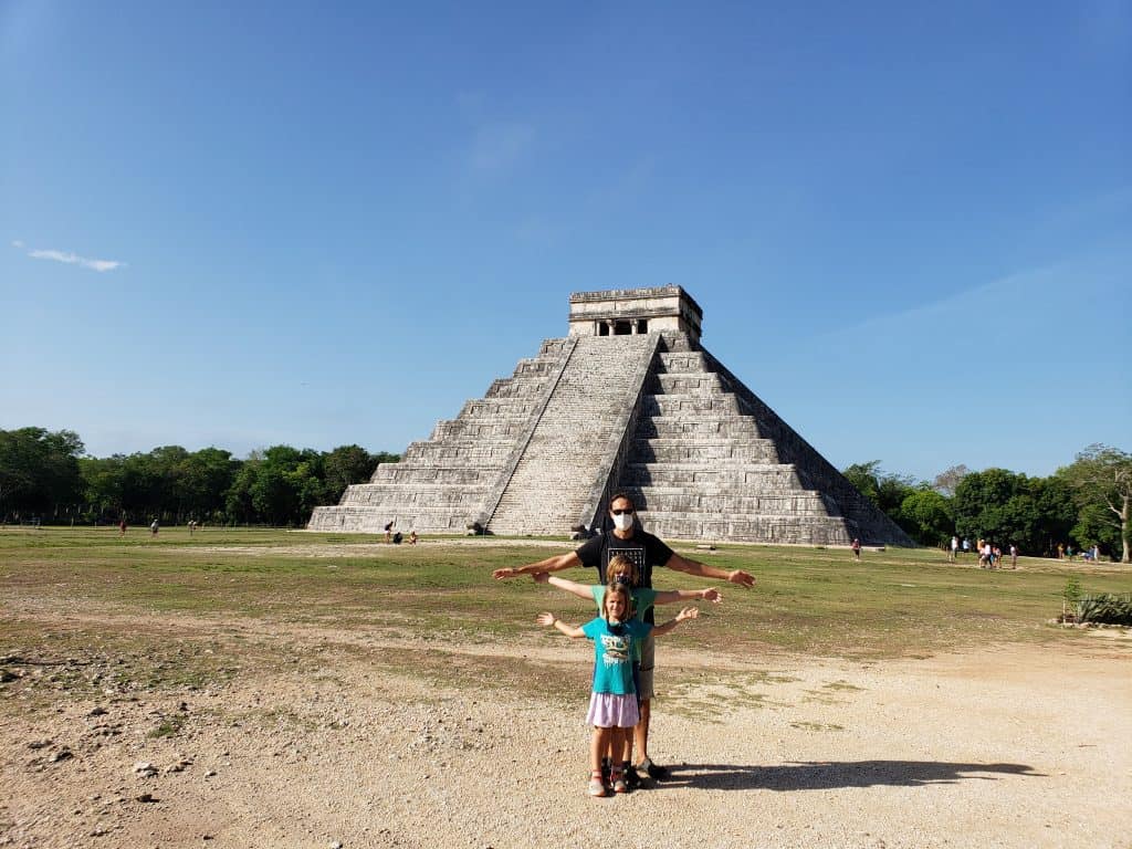family of two adults and two kids in front of chichen itza pyramid, arms outstretched