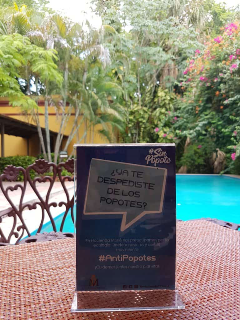 Sign in Spanish saying 'say no to straws'. On a table with blue swimming pool and green trees behind
