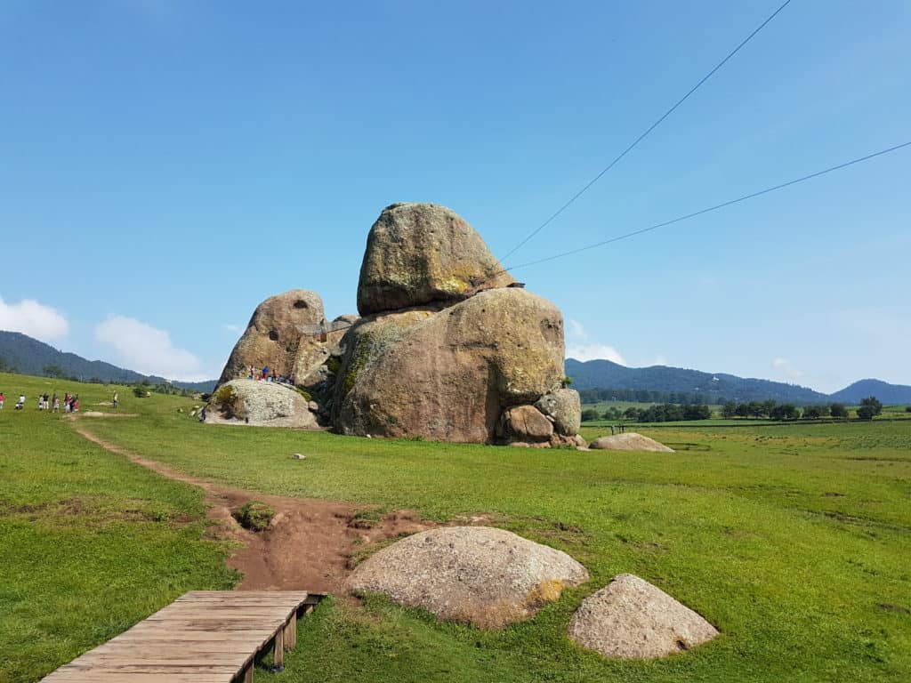 giant rocks, wooden path in left corner. grass and blue sky
