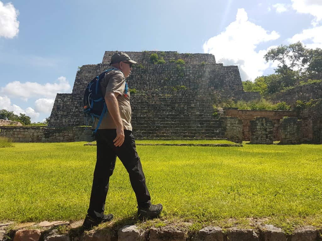 man walking toward a maya pyramid over grass