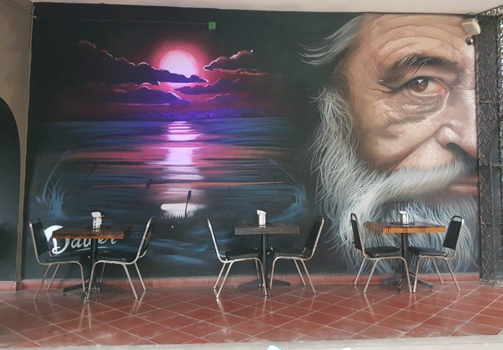 mural of old man with grey beard and hair. sunset mural next to him