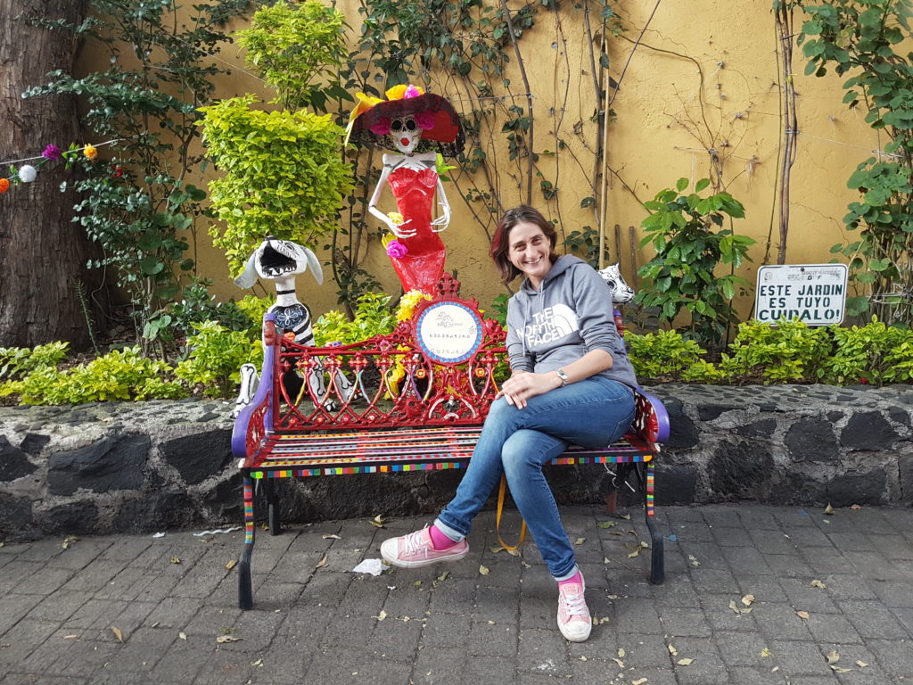 Cassie sitting on a bench with a catrina behind her