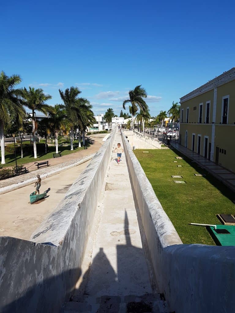 children running along a five hundred year old wall (permitted!). grass on one side, concrete on the other, palm trees, blue sky