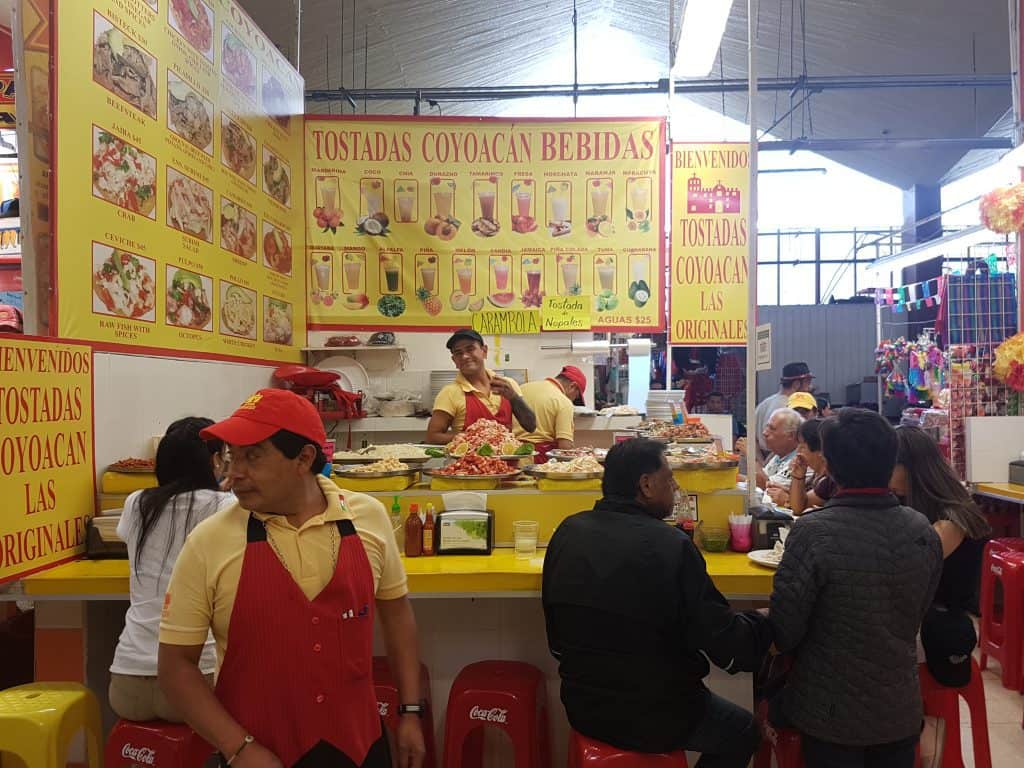 Food stall in market. Menus on wall, all yellow. Counter is yellow,staff wear yellow and red