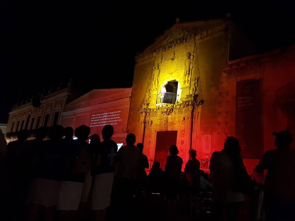 Old house lit up with red and yellow lights. Audience below in silhouette