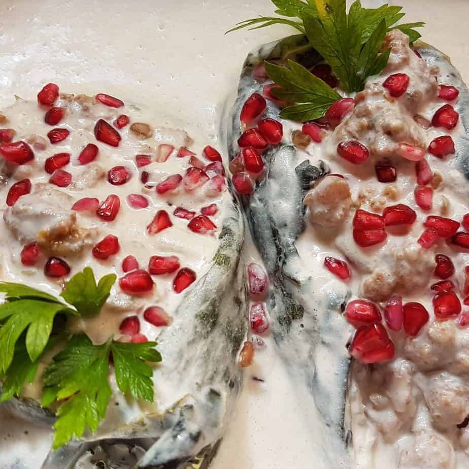 stuffed poblano chile with white sauce, red pomegranate seeds and parsley