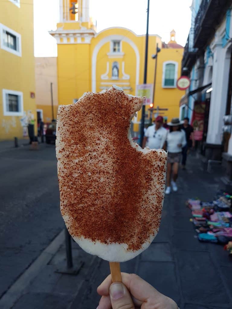 slice of jicama covered in red chile powder. Bites taken out. Yellow church in background