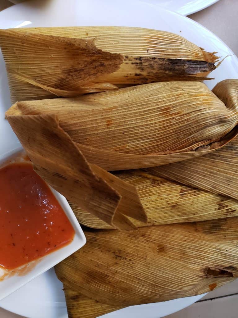 corn wrapped vegan tamales with small bowl of spicy red salsa