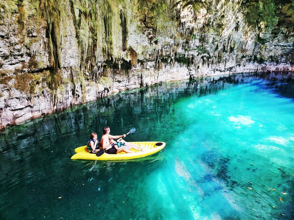 three people in a yellow kayak in water lit by the sun (in a cave)