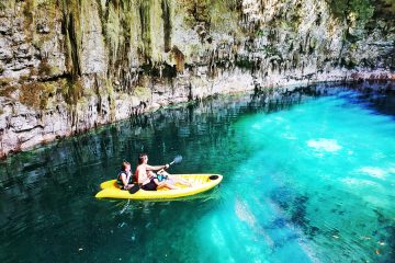 three people in a yellow kayak in water lit by the sun (in a cave)