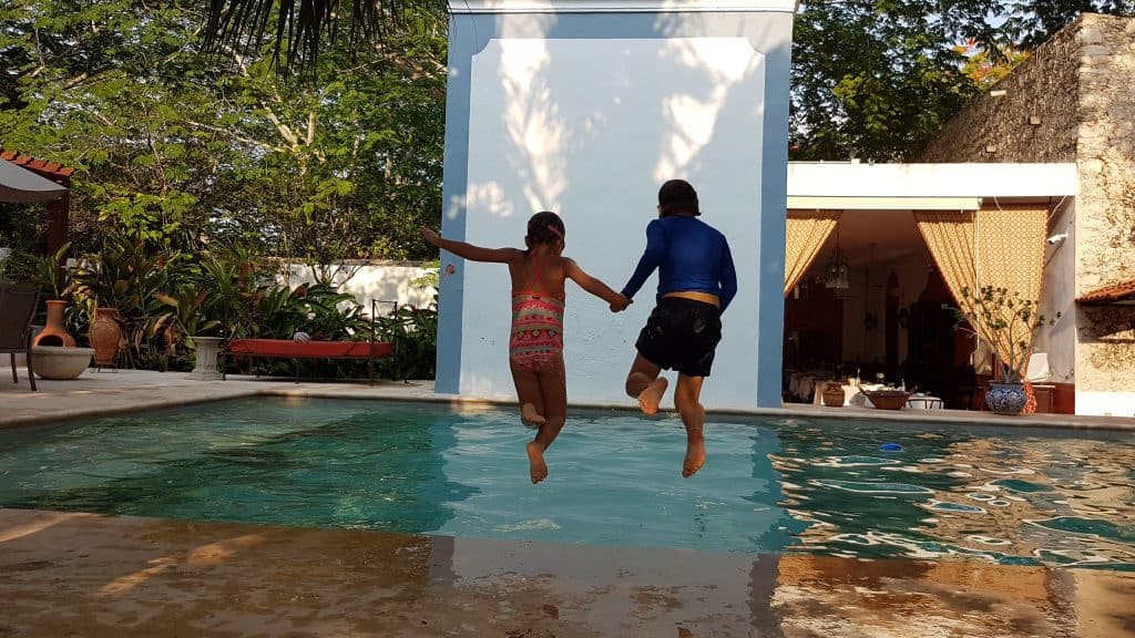 boy and girl holding hands and jumping into a pool. taken from the back
