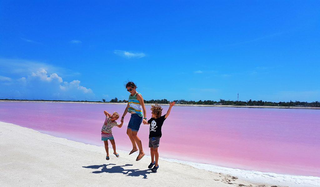 Cassie and two kids jumping in air in front of pink lake. v blue sky