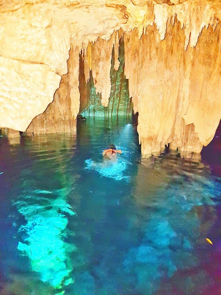 swimming in cave cenote - clear blue water, rock formations hanging down around solitary swimmer