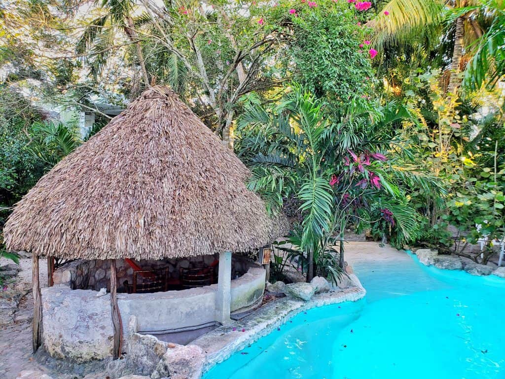bright blue swimming pool, round thatched hut and jungle all around