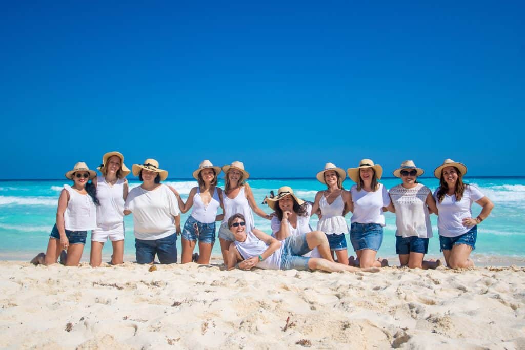 group of women kneeling together on beach with white sand, beautiful turquoise sea and blue sky