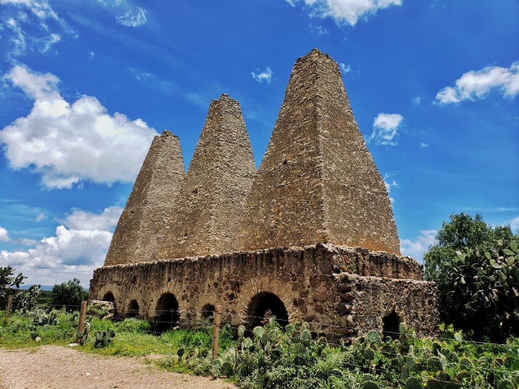 three large brick pyramidal ovens in a row. cacti at their base. blue sky