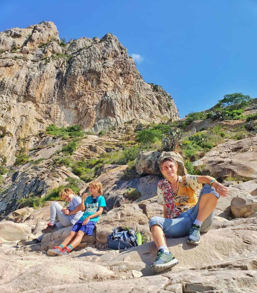 woman in two kids sitting on rocks, mountain towering behind