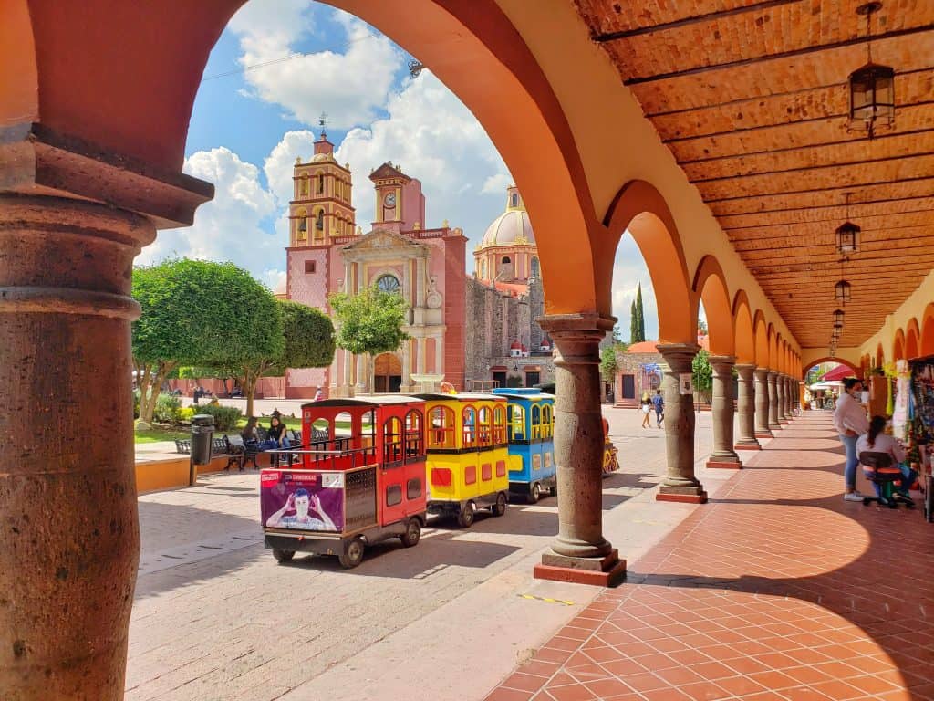 looking at a children's train and church in background from under a run of arches