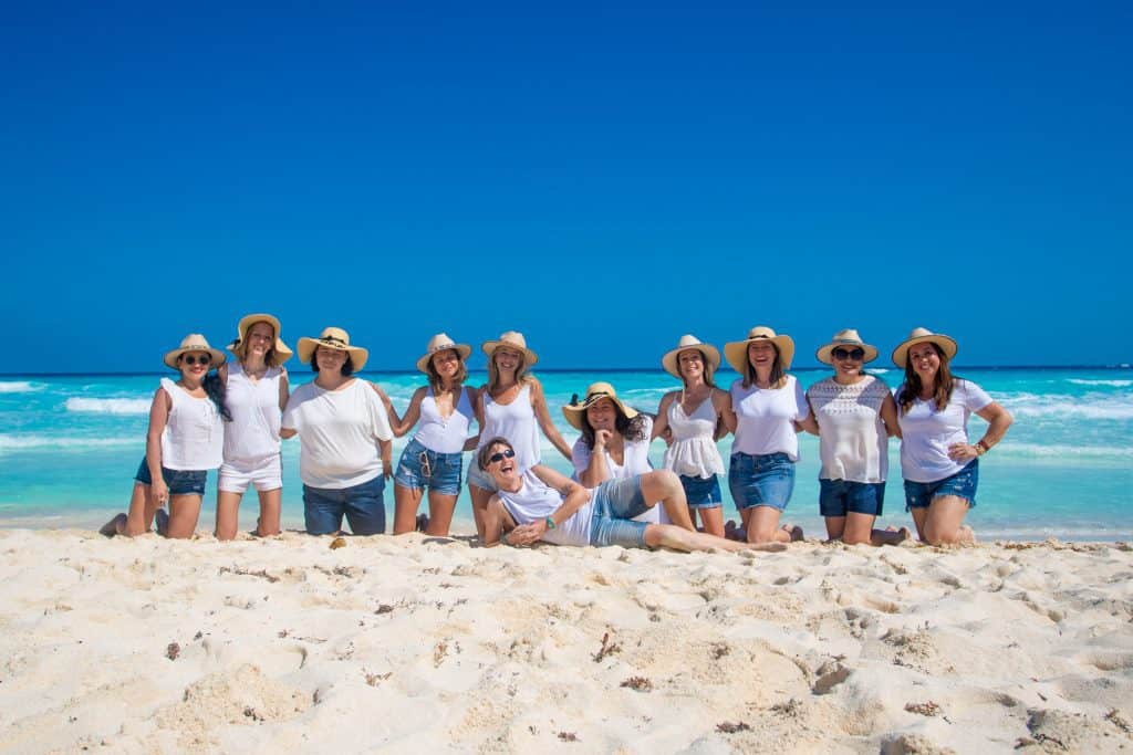 group posing on beach wearing white. 