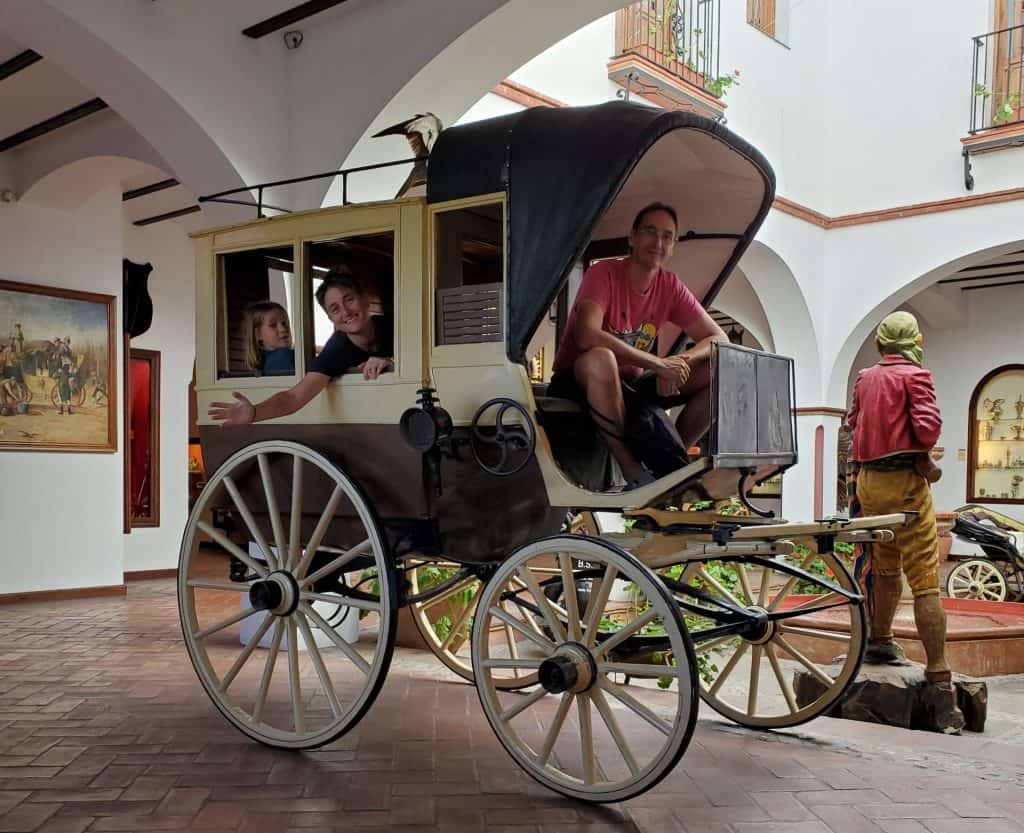 two adults and a kid in an old fashioned carriage in a museum