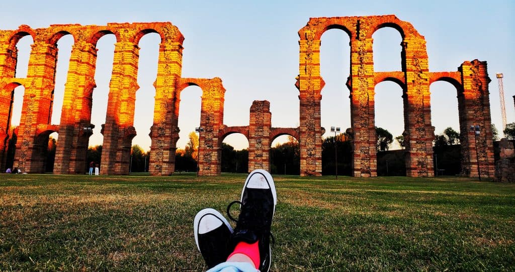 arches from a tall aqueduct. Crossed feet with pink socks and black converse in foreground