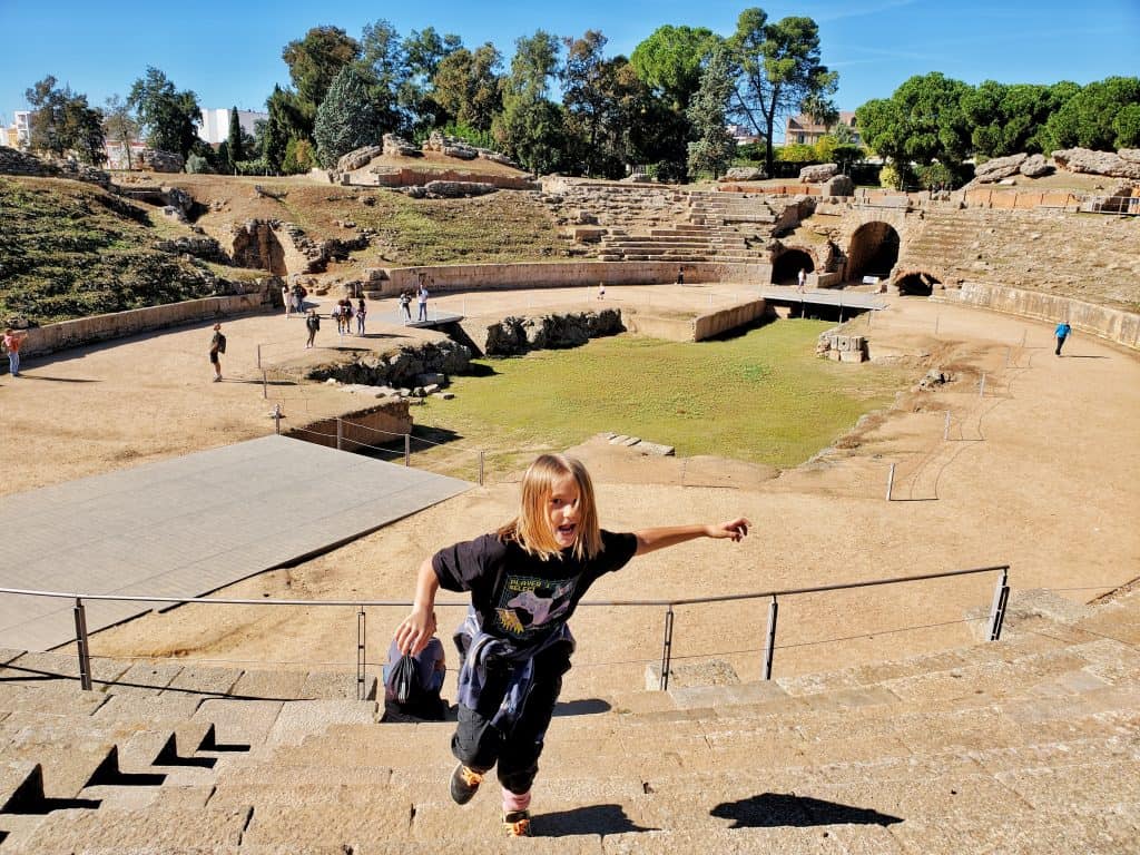 child in black running up the seats of amphitheatre, grass area in background