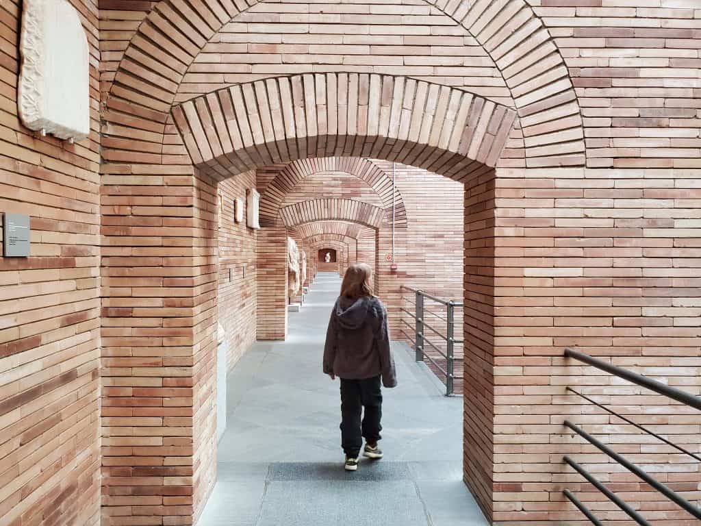 child in dark clothes walking under modern brick arch