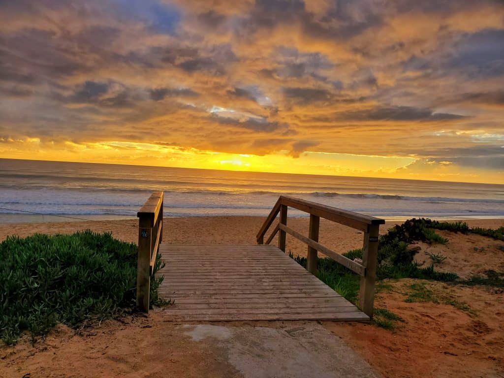 small wooden walkway down to sandy beach at sunset