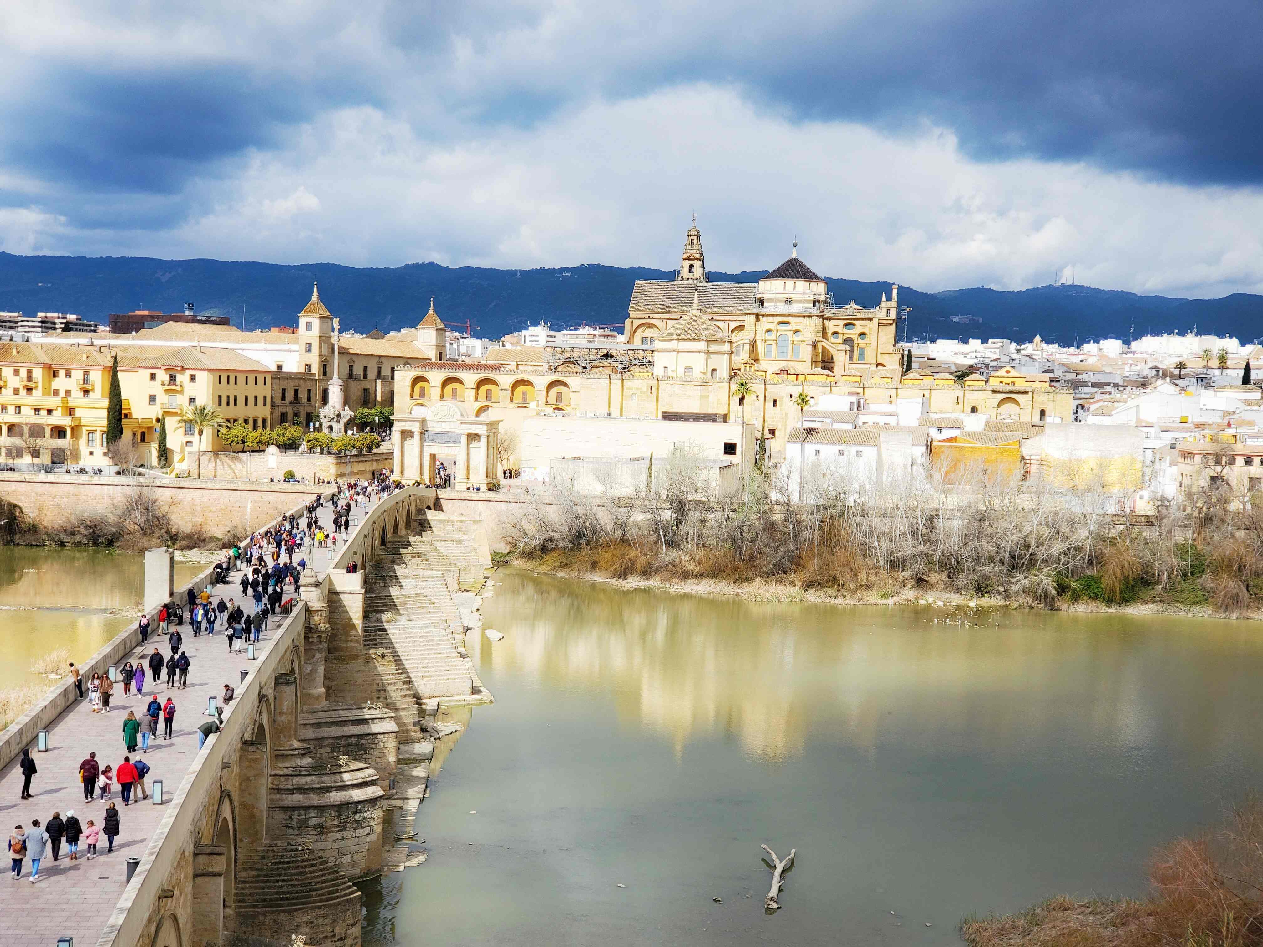 view from above Cordoba's roman bridge, river, mezquita in distance, grey clouds