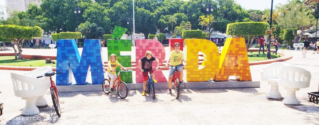 adult and two kids on bikes in front of colourful Mérida letters