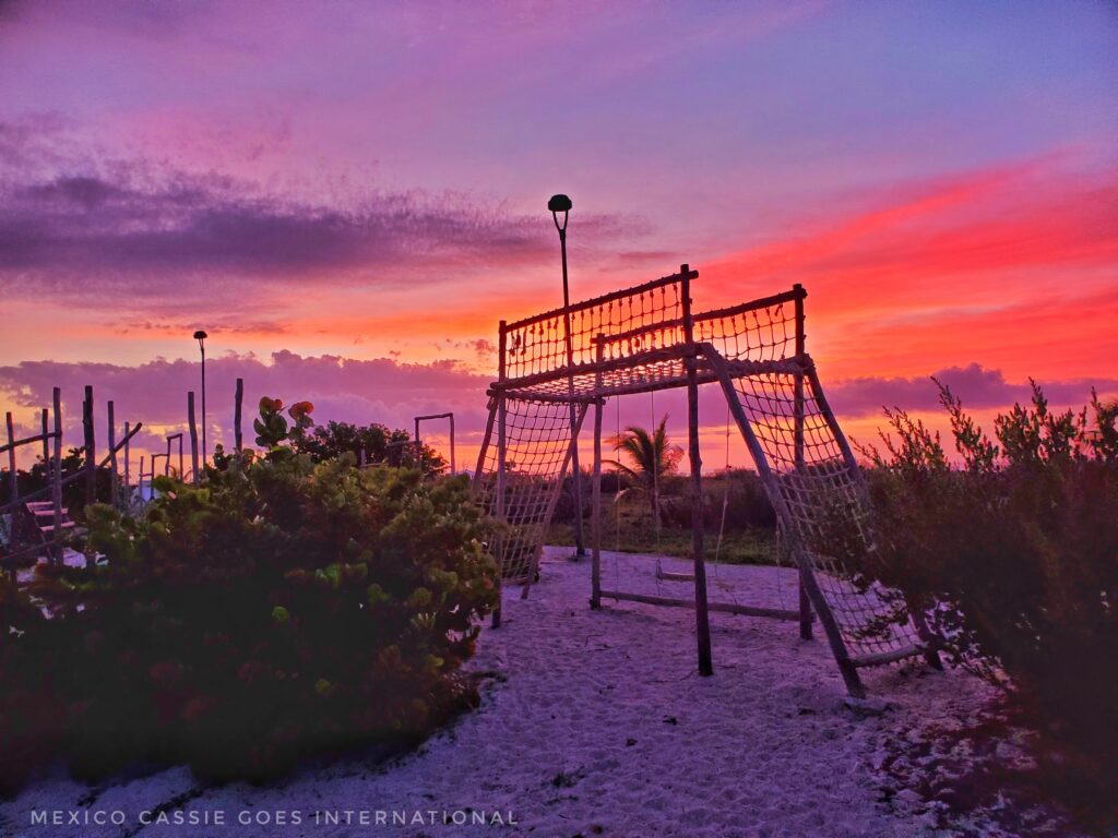 deep pink and orange sunset behind rope and wood climbing frame on beach