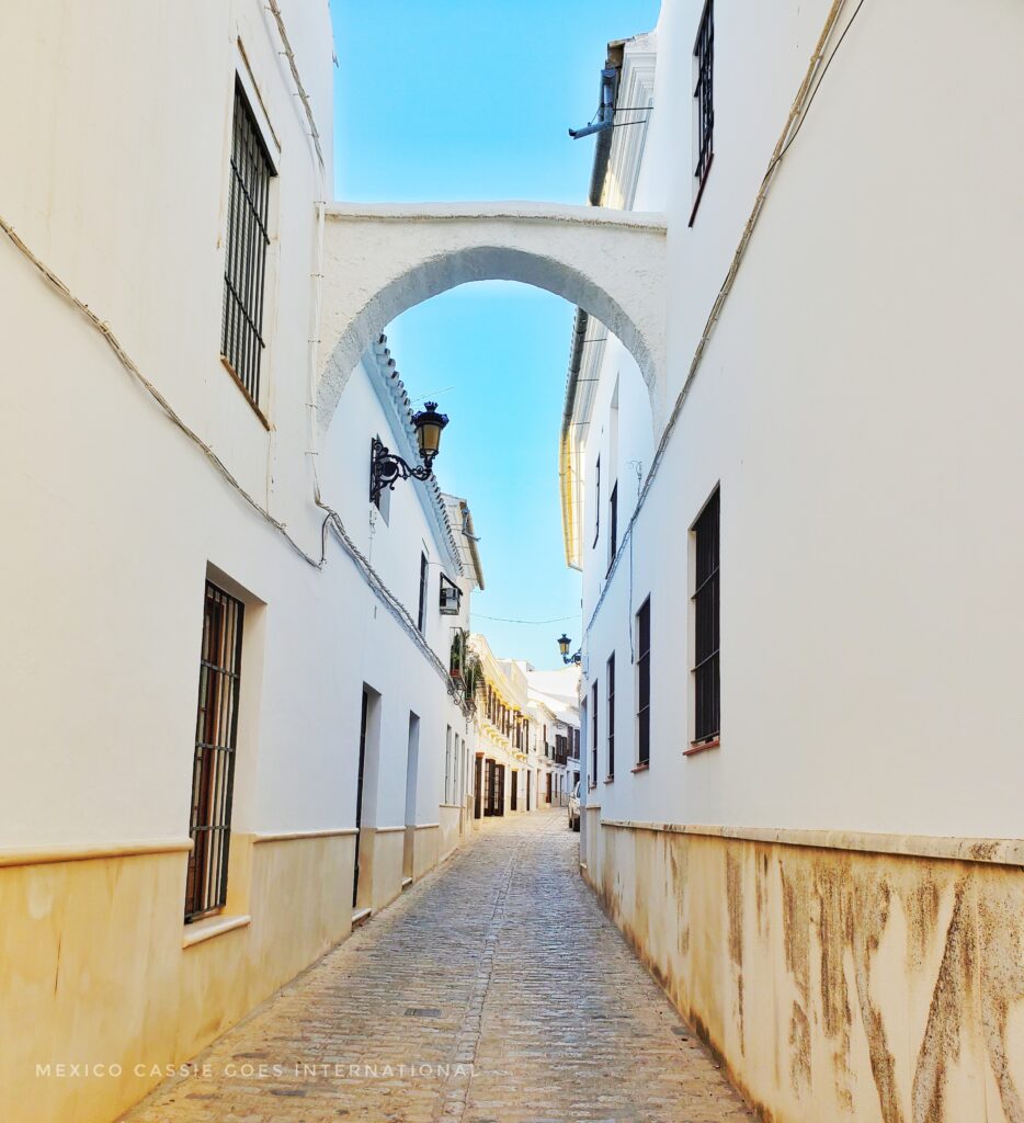 view down a narrow empty street with an arch overhead. All buildings are white