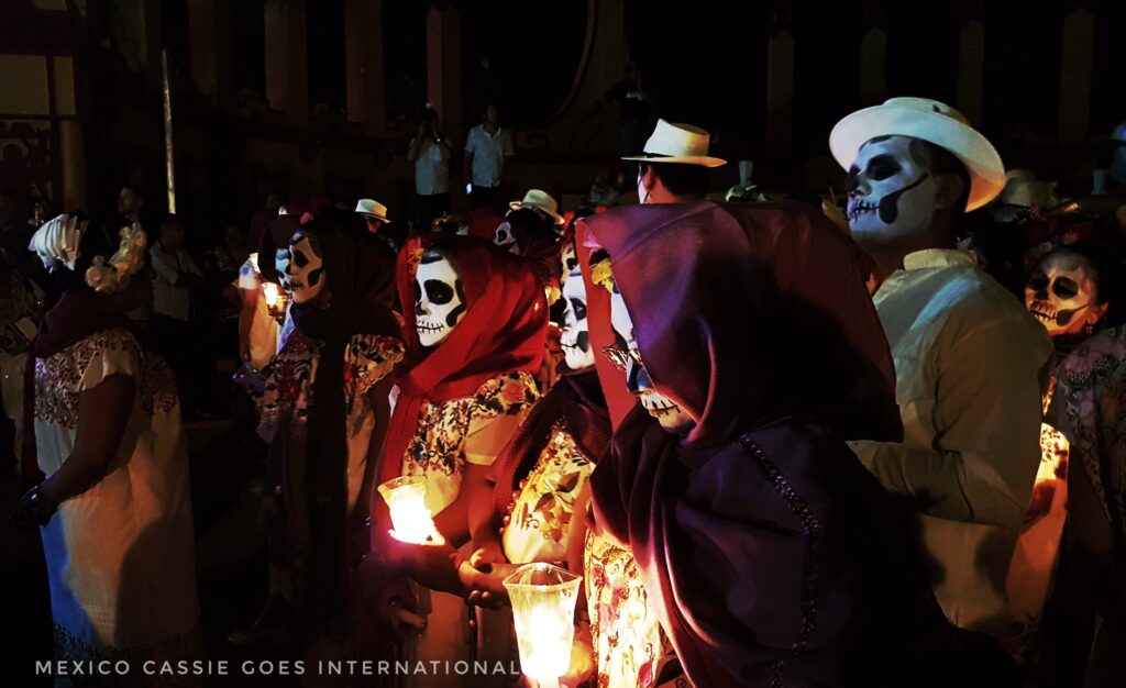 group of people with faces painted as skeletons. Holding candles. Dark