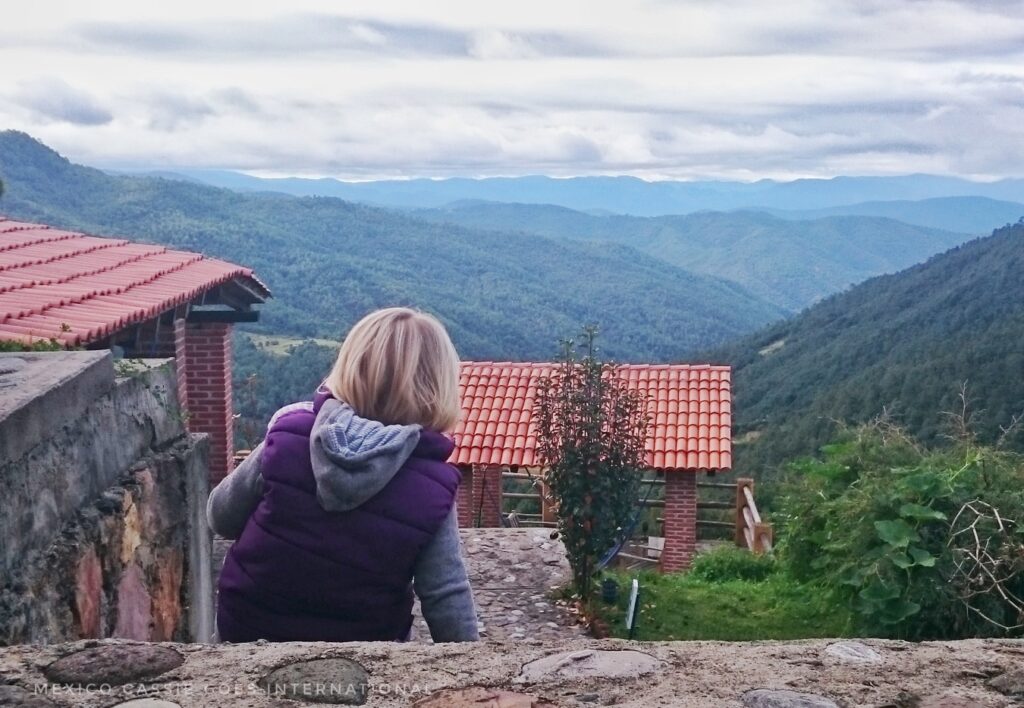 kid in purple with back to camera sitting on step looking out at view over red roofs, green hills and cloudy sky