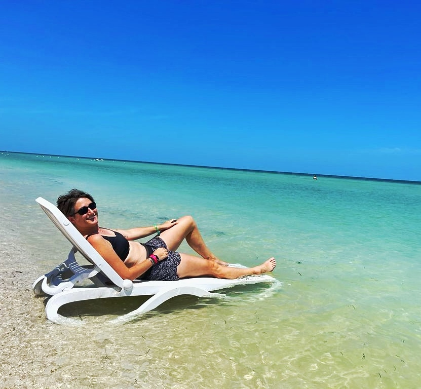 Cassie lying on a white plastic lounger in the ocean - clear green water, bright blue sky