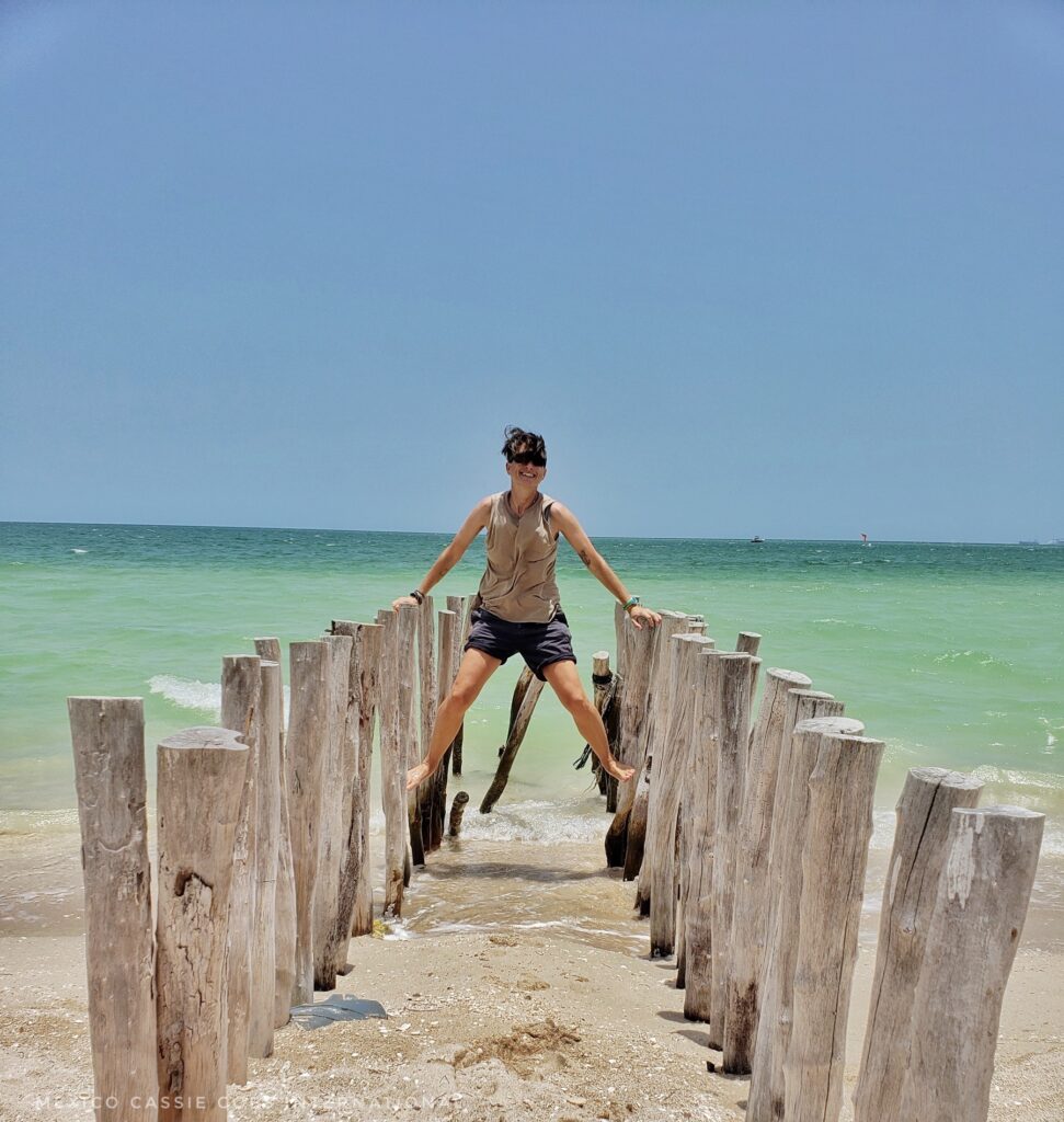 wooden posts sticking out of sand. green sea and blue sky. person holding self up on posts