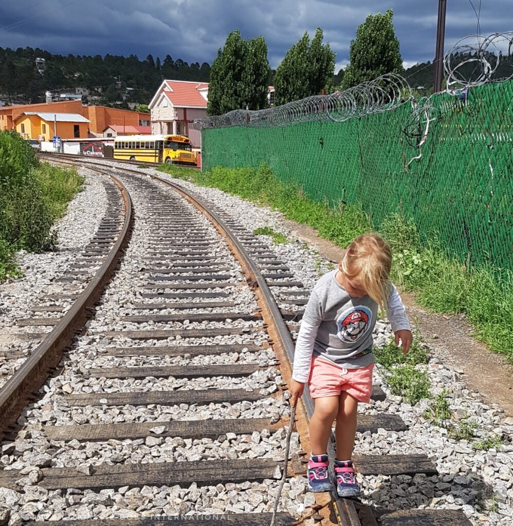 small girl in foreground looking down. walking on train tracks