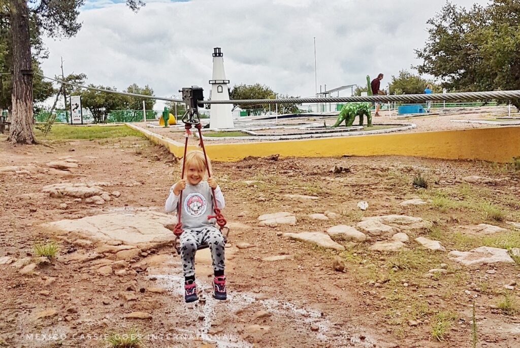 small child on a low zipline over muddy ground
