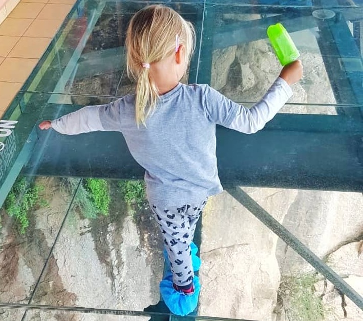 small child walking on a glass floor holding a green popsicle