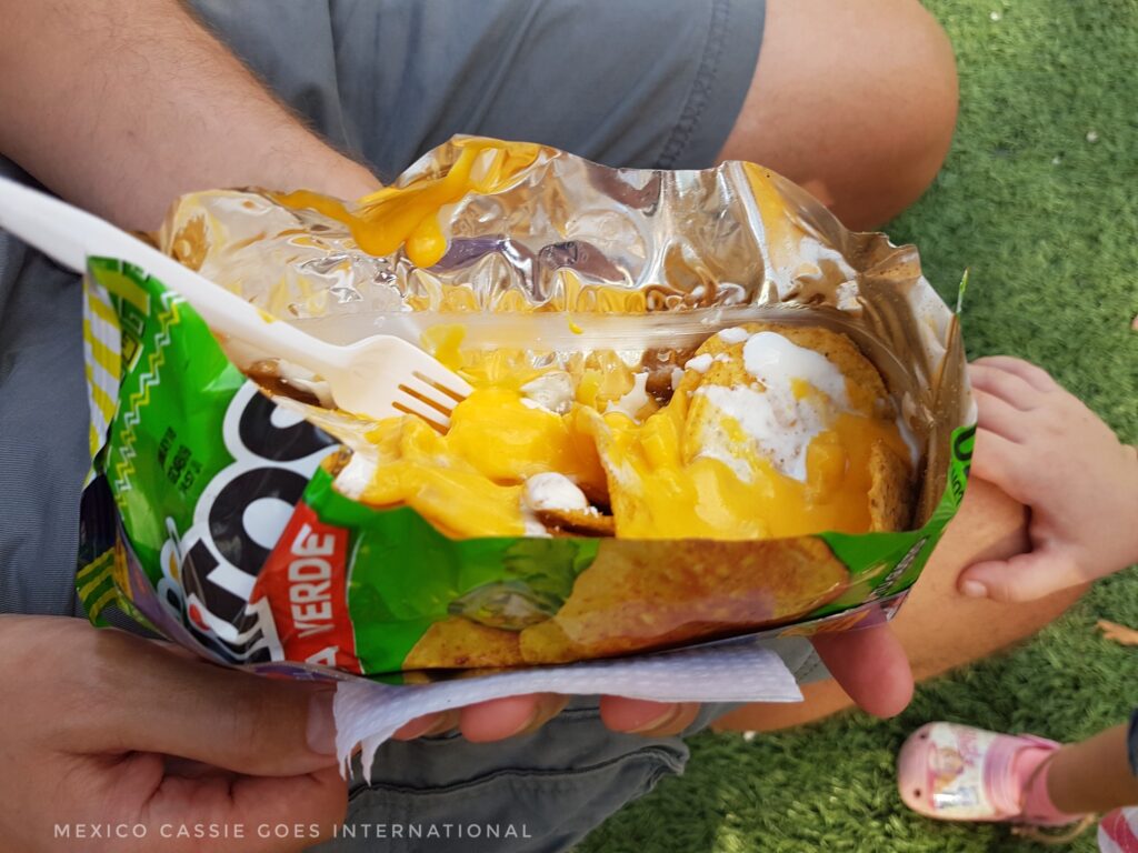 bag of tostilocos (nachos) opened length ways, chips covered in liquid cheese. plastic fork in bag