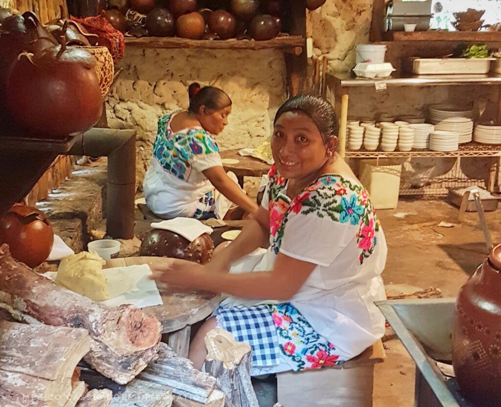 two women in traditional Maya dress making tortillas by hand