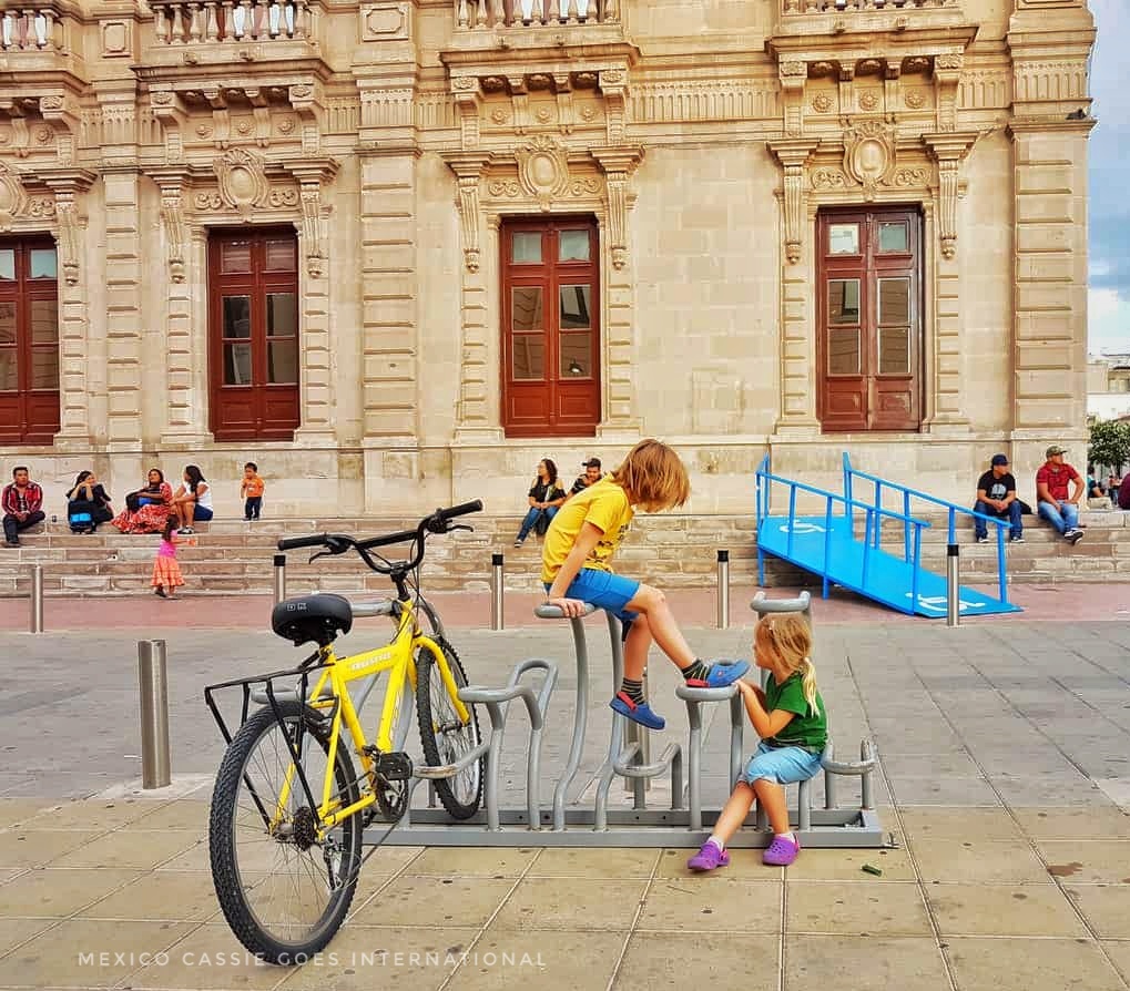 two small kids playing on a bike rack. yellow bike there